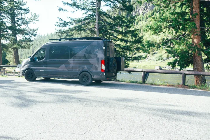 A dark gray Flatlander camper van, an ideal rv rental, by a scenic river and towering trees. Perfect for adventure travel.. Vandoit Vandoit Class B 2020