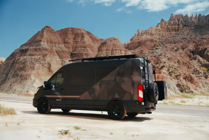 Customized dark RV rental van with a geo pattern and roof rack parked in rugged badlands terrain.. Vandoit Vandoit Class B 2020
