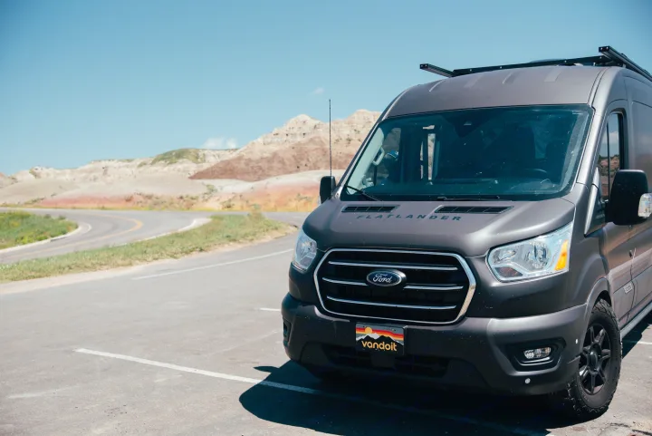 A dark gray Flatlander rv rental van is parked on asphalt, facing a scenic road and colorful badlands mountains under a blue sky.. Vandoit Vandoit Class B 2020