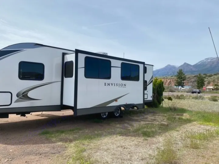 This white Envision rv rental travel trailer, with slide-out extended, enjoys a beautiful scenic mountain backdrop.. Gulf Stream Gulf Breeze 2023