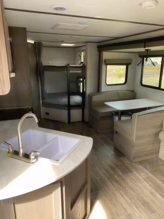 Modern RV rental interior showing a kitchen with sink, dinette, and bunk beds. Ideal for family trips.. Gulf Stream Gulf Breeze 2023