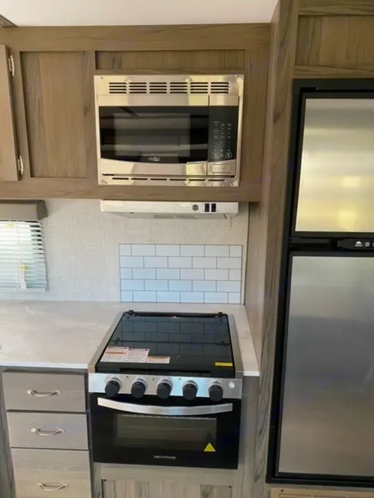 Stainless steel microwave, gas stove, and fridge in a compact RV rental kitchen.. Gulf Stream Gulf Breeze 2023