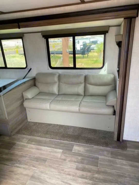 RV rental interior featuring a light gray reclining sofa, large windows, and sleek wood-look laminate flooring.. Gulf Stream Gulf Breeze 2023