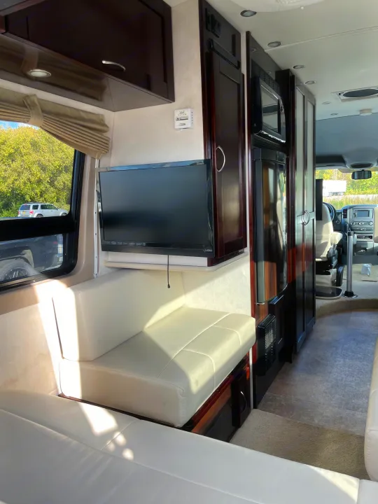 Spacious RV rental interior with TV, cream seating, dark wood cabinets, and appliances like a refrigerator.. Pleasure-Way Pleasure-Way Class B 2013