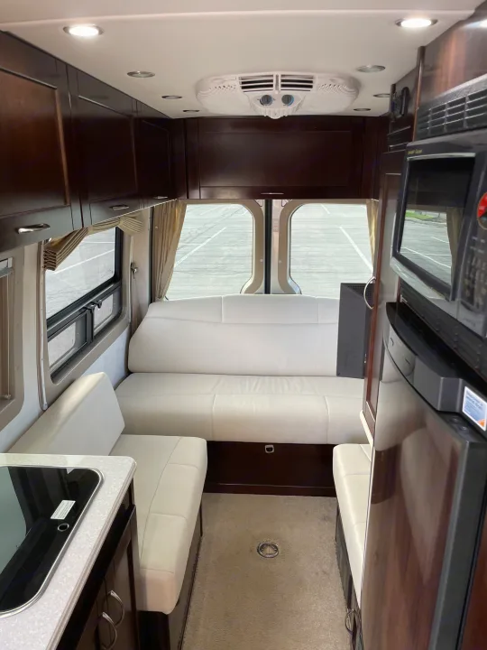 Inside a luxurious RV rental: sleek white seating, dark wood cabinets, kitchenette, microwave & fridge. Ideal for road trips.. Pleasure-Way Pleasure-Way Class B 2013
