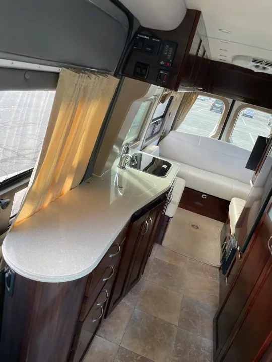 Inside a premium RV rental: kitchenette with sink, elegant wood cabinets, and rear sofa seating. Ideal for travel.. Pleasure-Way Pleasure-Way Class B 2013