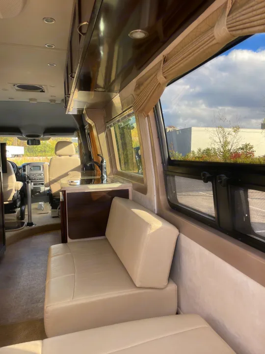 RV rental interior shows light beige seating, a compact kitchenette, and large windows looking outside.. Pleasure-Way Pleasure-Way Class B 2013