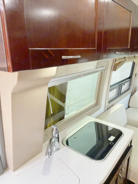 Compact RV rental kitchen features dark wood cabinets, a sleek sink, and a black glass cooktop next to a large window.. Pleasure-Way Pleasure-Way Class B 2013
