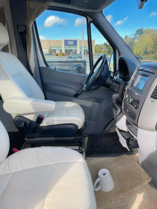 Glimpse inside an RV rental: White leather seats, driver's area controls, and a clear view of a Garden Center building.. Pleasure-Way Pleasure-Way Class B 2013