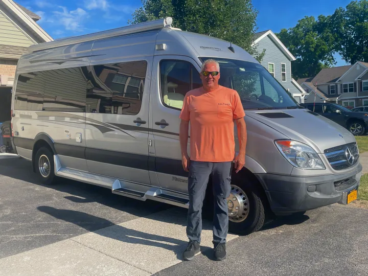A man stands proudly beside a sleek silver Pleasure Way Plateau RV rental, ready for his next adventure.. Pleasure-Way Pleasure-Way Class B 2013