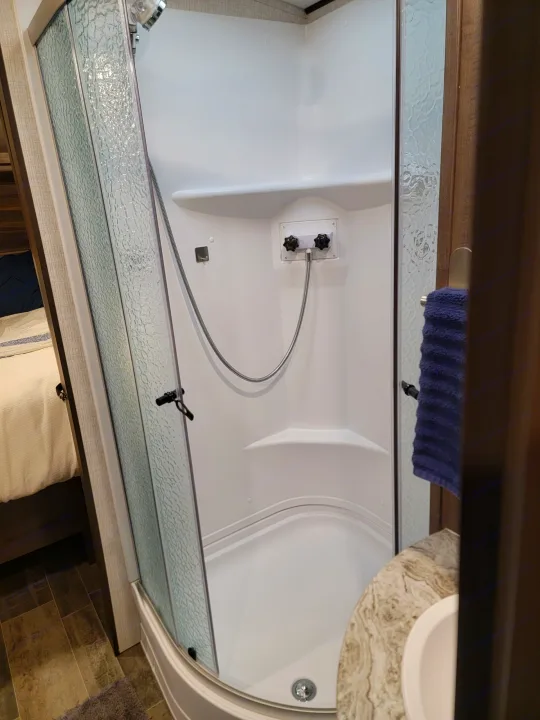 Clean, compact RV rental shower with textured glass door, handheld shower, easy-to-use controls, and integrated shelf.. Crossroads RV Sunset Trail Super Lite 2021
