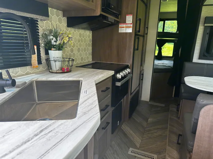 Inside a clean RV rental: kitchen with sink, stove, microwave, fridge, and dining table. Bunk beds visible in background.. Highland Ridge RV Olympia 2022
