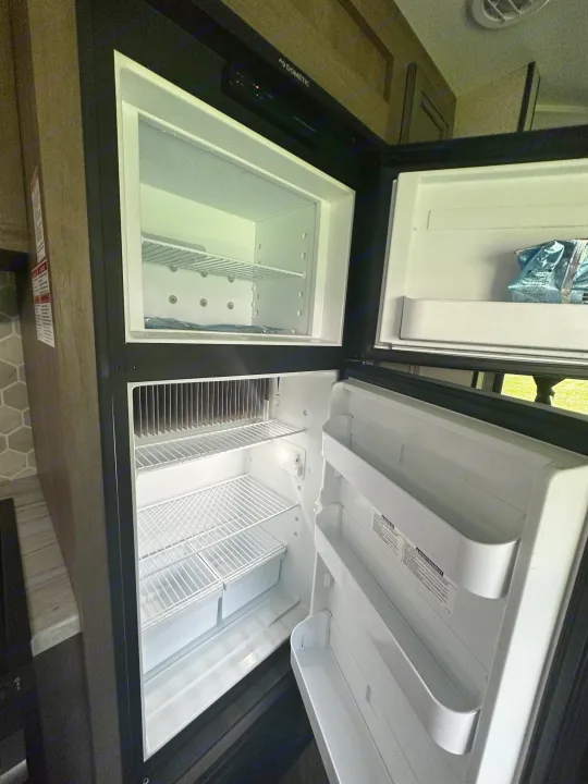 Inside an RV rental: an empty Dometic refrigerator and freezer with wire shelves, ready for your trip.. Highland Ridge RV Olympia 2022