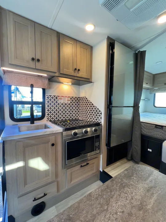 Modern rv rental interior featuring a compact kitchen with a sink, stove, and microwave, next to a cozy sleeping area.. Forest River Sunseeker 2025