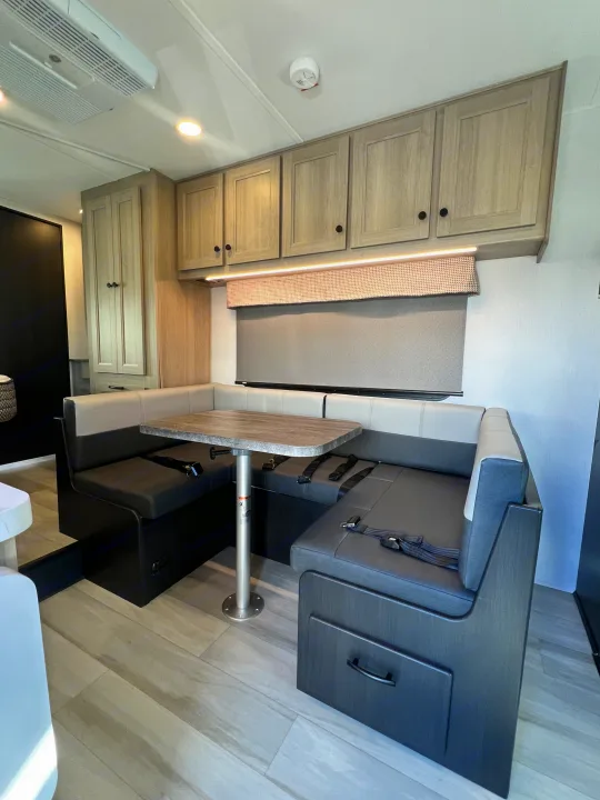 Spacious rv rental dinette with U-shaped two-tone seating, table, overhead cabinets, and LED lighting. Ideal for dining.. Forest River Sunseeker 2025
