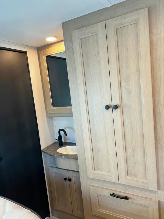 Inside an **rv rental**, a compact bathroom vanity area features a sink, black faucet, mirror, and light wood cabinets.. Forest River Sunseeker 2025