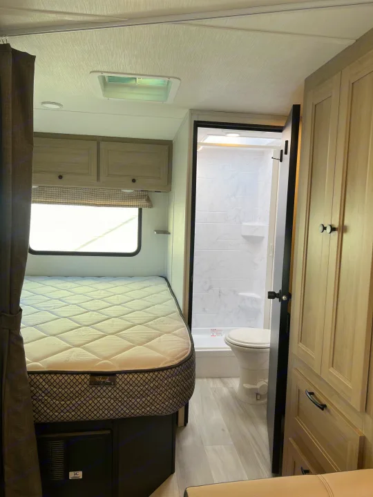 Inside a compact rv rental: a cozy bedroom with mattress on the left and an open bathroom with a shower and toilet on the right.. Forest River Sunseeker 2025