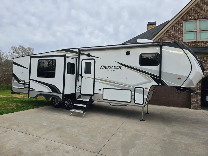 This Crusader Lite fifth-wheel RV rental, parked on a driveway with steps extended, is ready for your next travel adventure.. Crusader Lite 2022