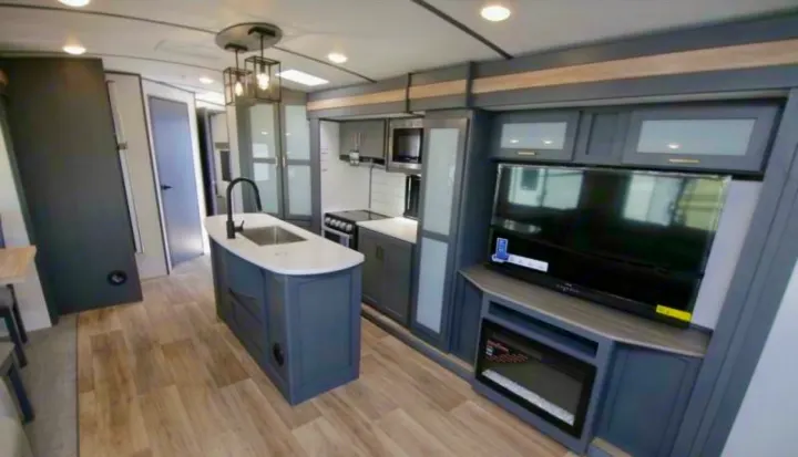Spacious modern RV rental interior featuring a full kitchen with island sink, stove, living area with TV, and electric fireplace.. Keystone RV Bullet Premier Ultra Lite 2022