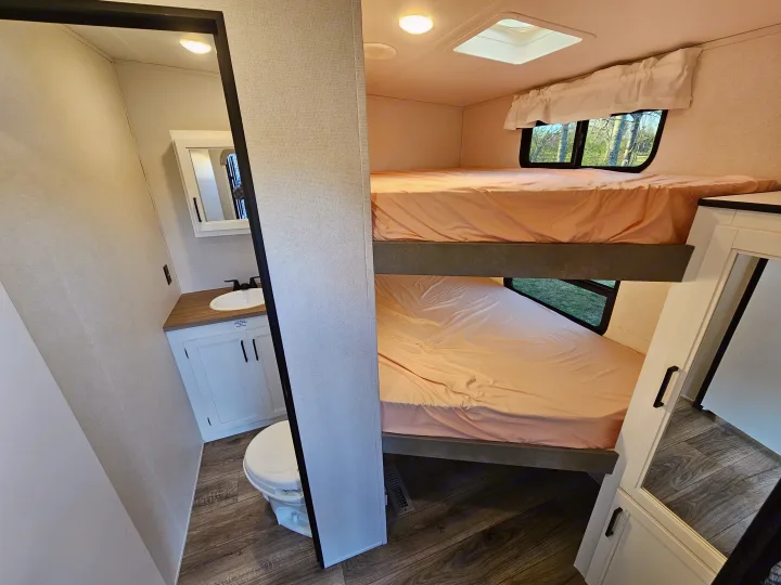An RV rental interior: compact bathroom with toilet and sink, adjacent to cozy bunk beds.. Crusader Lite 2022