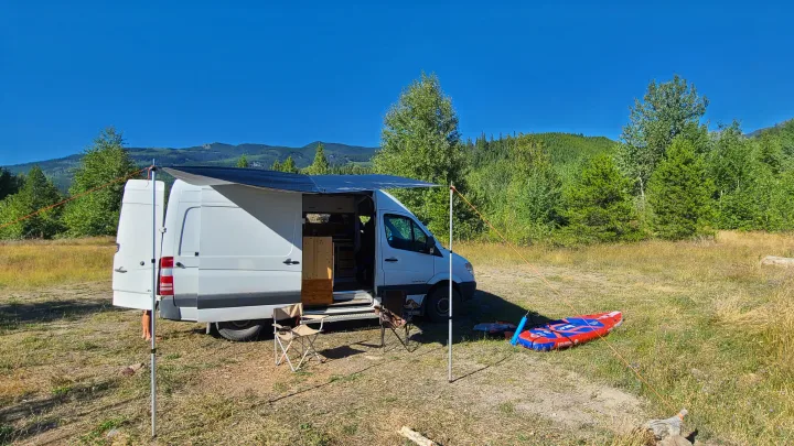 RV rental camping setup: white van with an awning, chairs, and inflatable paddleboard. Scenic mountain view.. volkswagen sprinter 2007