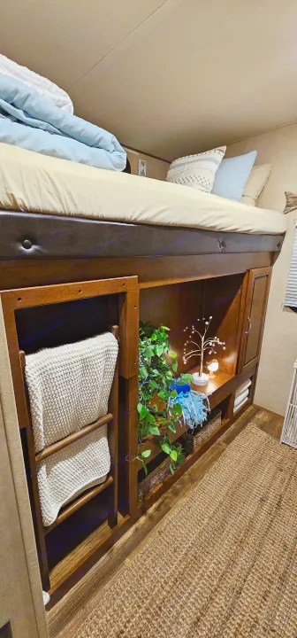 Inside an RV rental: a cozy bunk bed above organized storage shelves with blankets, plants, decor, & woven baskets.. Forest River Vibe 2017