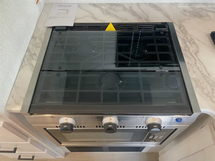 RV rental: A clean, modern Greystone gas stovetop and oven unit with a glass top, control knobs, and an owner's manual.. East To West Entrada 2025
