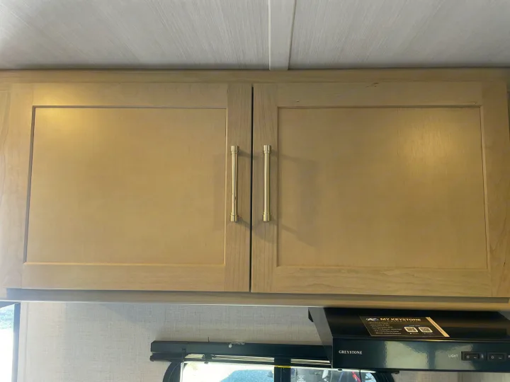 Overhead light wood cabinets with handles and a range hood in an rv rental kitchen interior, offering storage for your journey.. Keystone Springdale Classic Mini 2024
