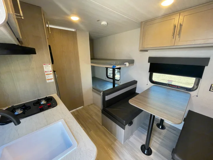 RV rental interior shows a compact kitchen with stove/sink, a dinette with table, bunk beds, and overhead cabinets.. Keystone Springdale Classic Mini 2024