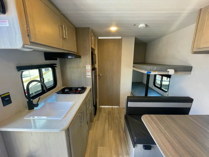 Inside an RV rental: bright kitchen with sink & stovetop, plus comfy dinette and cozy bunk beds.. Keystone Springdale Classic Mini 2024