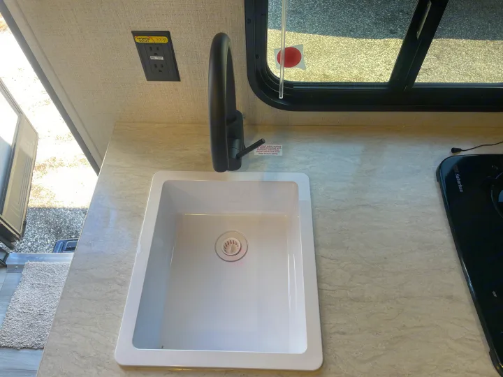 RV rental kitchen: A white sink, black faucet, GFCI outlet (solar ready), and stovetop on a light countertop.. Keystone Springdale Classic Mini 2024