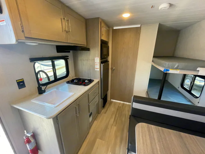 Inside this **rv rental**, find a compact kitchen with sink/stove, dinette, and rear bunk beds, ideal for travel.. Keystone Springdale Classic Mini 2024