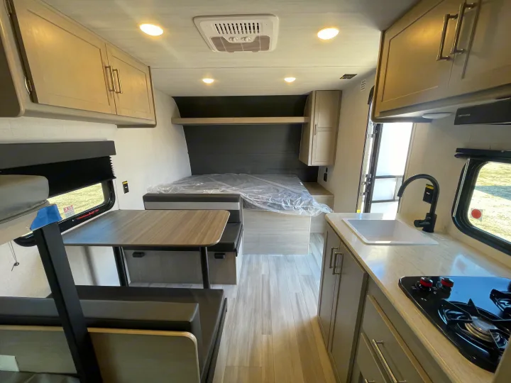 Modern RV rental interior with light wood cabinetry, kitchen, dinette, and bunk beds, offering compact living space.. Keystone Springdale Classic Mini 2024