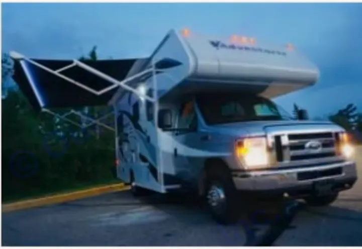 A grey and white Class C RV rental, with a large, lit awning unfurled, sits parked at dusk, ready for adventure.. Adventurer Adventurer Motorhome 2019