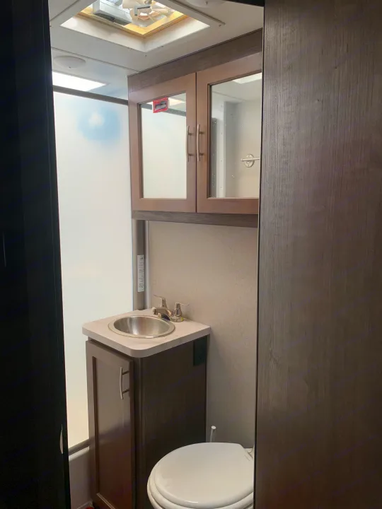 An RV rental's compact bathroom showing a shower, sink, toilet, and overhead cabinets. Perfect for camping trips.. Adventurer Adventurer Motorhome 2019