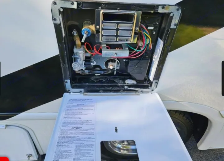 RV water heater's exterior access panel is open on an RV rental, showing internal gas, burner, and electrical parts.. Thor Freedom Elite 2022