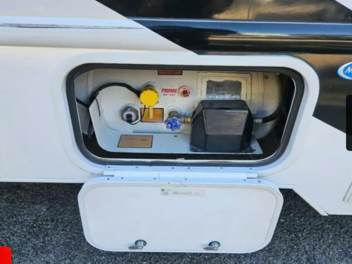 Open utility access panel on an RV rental, revealing the on-board propane tank with its yellow and blue valves and black regulator.. Thor Freedom Elite 2022