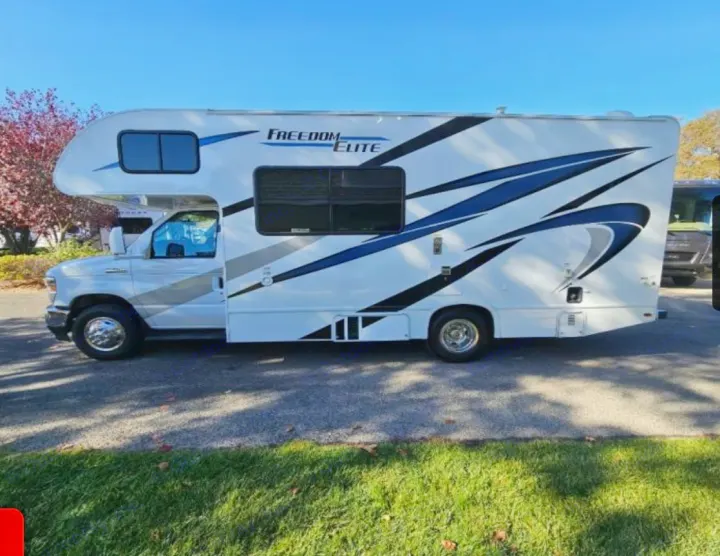 White Freedom Elite Class C **rv rental** with bold blue & black graphics, parked on pavement. Ready for your adventures!. Thor Freedom Elite 2022