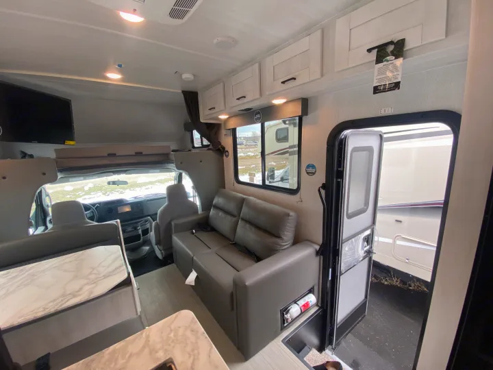 Step inside this rv rental: a modern motorhome living area with seating, table, and driver's cabin visible.. East to West Entrada 2025