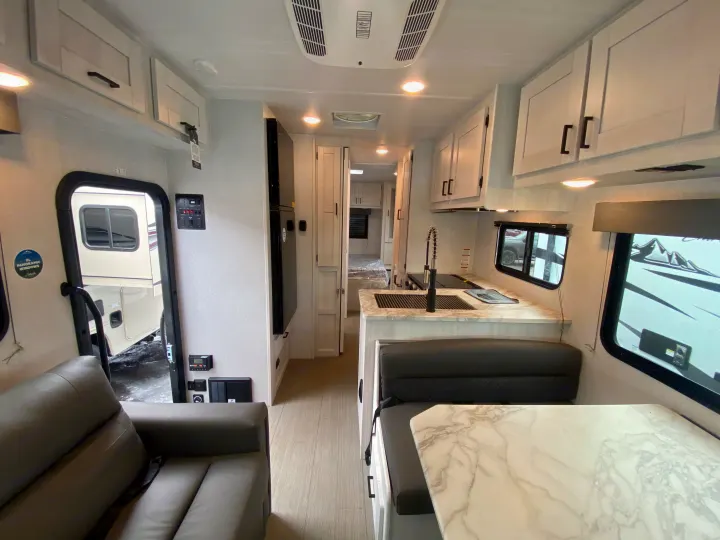 Spacious RV rental interior with a bright, modern kitchen, dining area, and comfortable grey sofa. Light-toned cabinets and flooring.. East to West Entrada 2025
