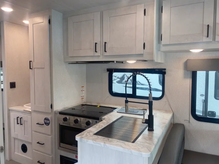 Modern RV rental kitchen. Features light wood cabinets, marble-look counters, stove, sink with pull-down faucet, and dinette seating.. East to West Entrada 2025