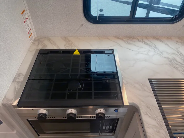 RV rental kitchen: gas range with glass cover, microwave/oven, and marble-look countertop. Sink with drying rack visible.. East to West Entrada 2025