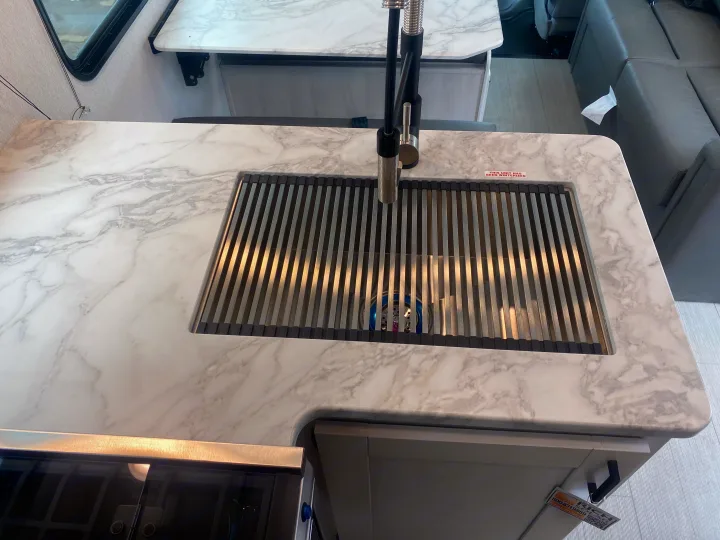 RV rental kitchen featuring a marble-look countertop, integrated sink with a drying rack, and modern faucet. A notice states the unit is winterized.. East to West Entrada 2025
