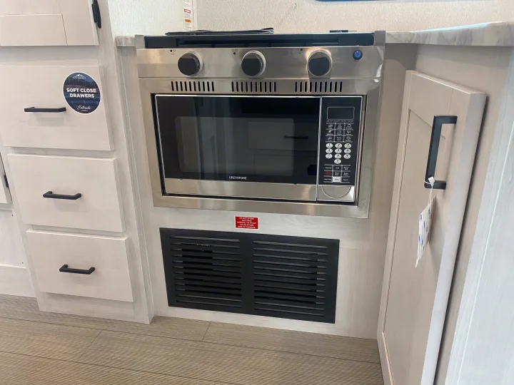 Compact RV rental kitchen featuring a stainless steel range with microwave below, light cabinets, and soft-close drawers.. East to West Entrada 2025