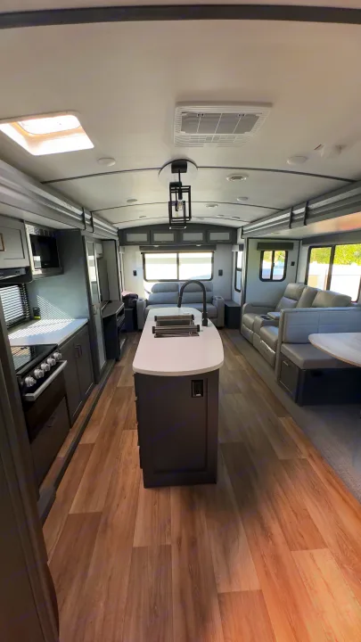 Spacious, modern RV rental interior featuring a kitchen island, comfortable living area, and dining nook with wood flooring.. Keystone RV Bullet Premier Ultra Lite 2022