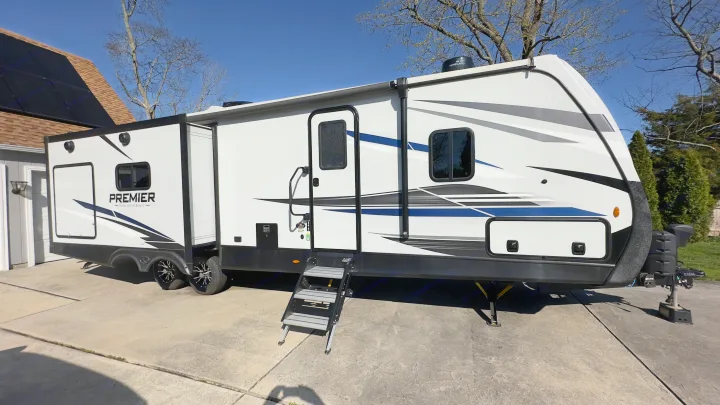 This large white RV rental, a travel trailer with blue/gray graphics and an extended slide-out, is parked on a driveway.. Keystone RV Bullet Premier Ultra Lite 2022