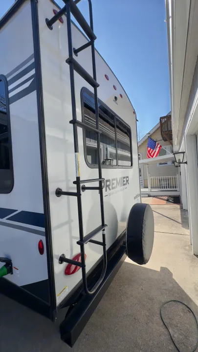 Rear view of a white Premier travel trailer, featuring a ladder & spare tire. Great for an rv rental adventure!. Keystone RV Bullet Premier Ultra Lite 2022