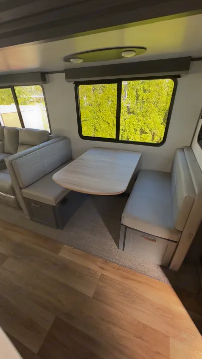 Bright RV rental dinette: light grey benches with storage, wood table, and green views from large windows.. Keystone RV Bullet Premier Ultra Lite 2022