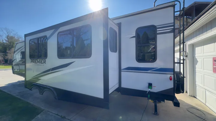 Brightly lit white RV rental, a Premier travel trailer, parked with its slide-out extended next to a garage.. Keystone RV Bullet Premier Ultra Lite 2022