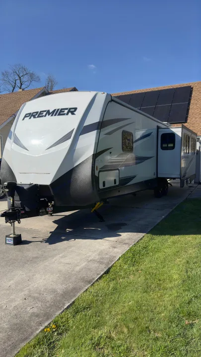 Sunny white Premier travel trailer parked on a concrete driveway, ready for an RV rental. House with solar panels in background.. Keystone RV Bullet Premier Ultra Lite 2022